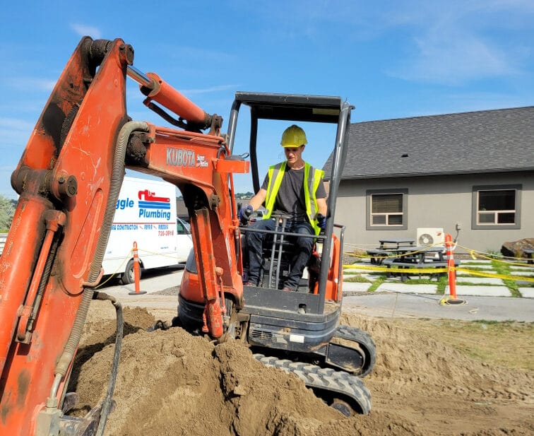 residential remodel Construction worker operating orange excavator on site.